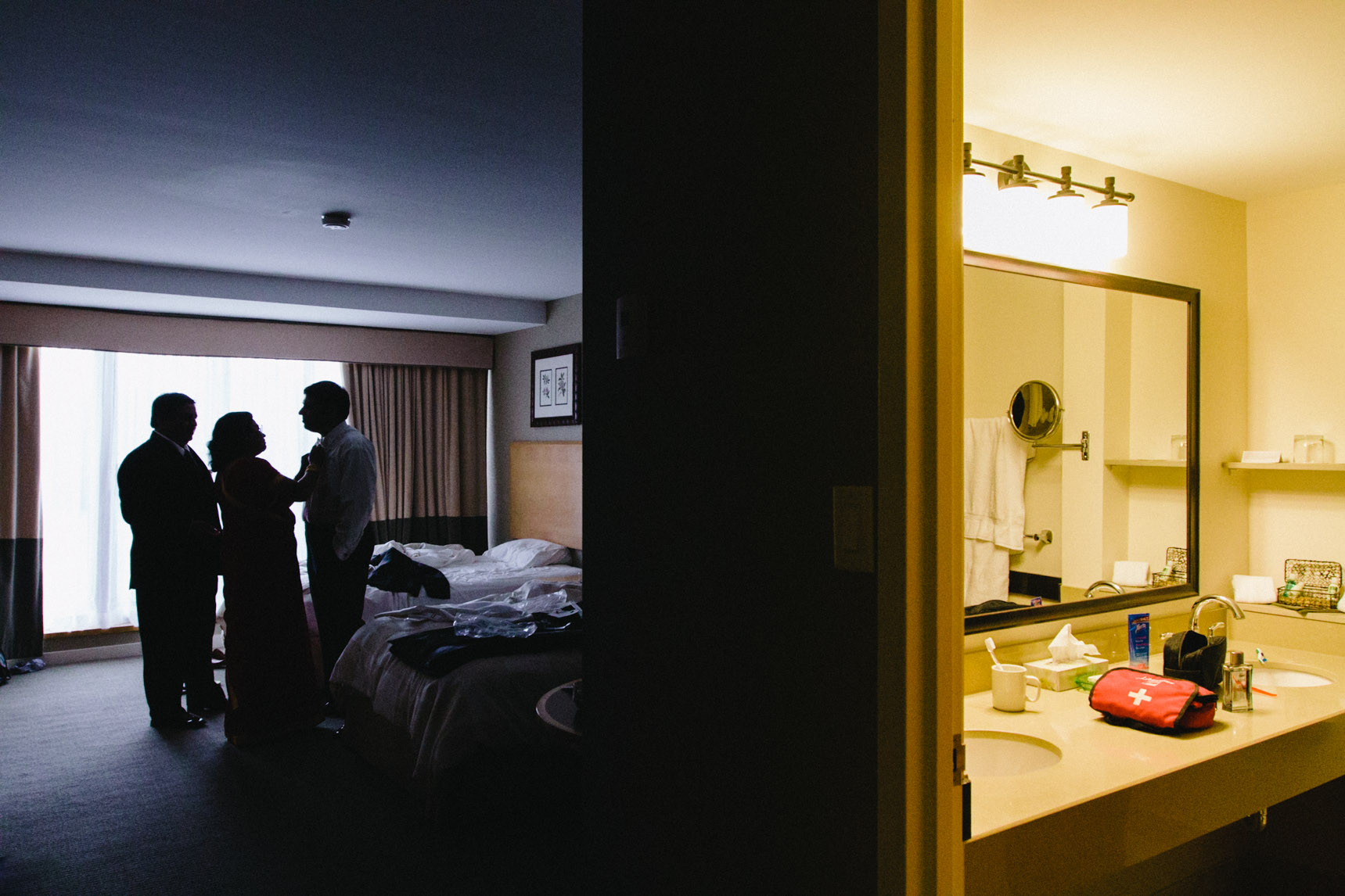Groom's parents help him prepare in hotel room of Kingbridge Centre.