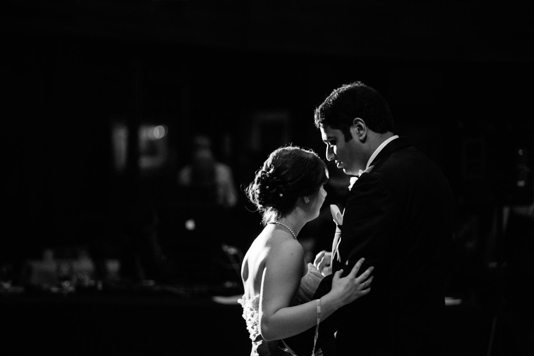 Bride and groom share a final dance, in profile, dramatic lighting.