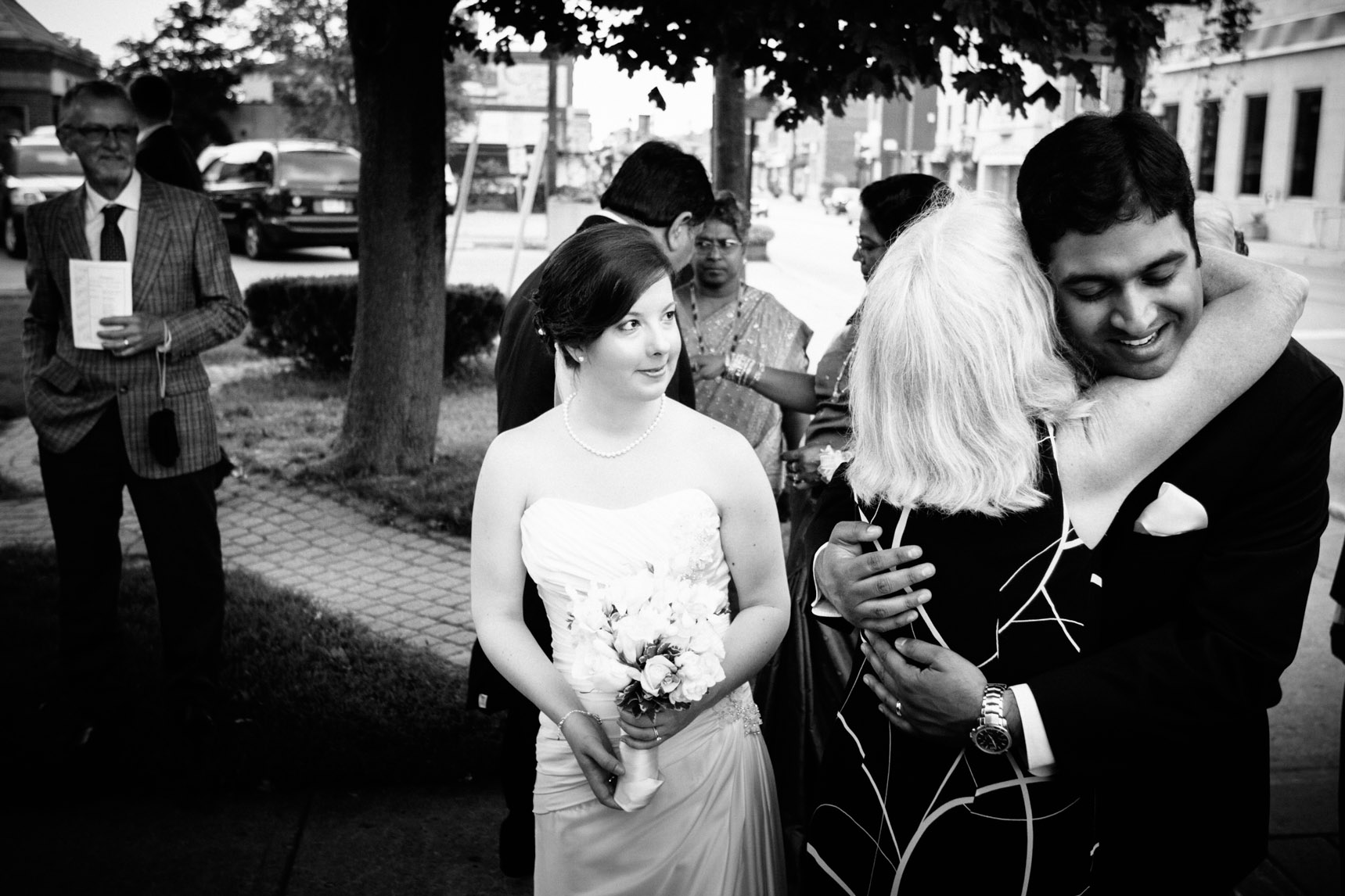 Bride watches the groom hug a wedding guest.