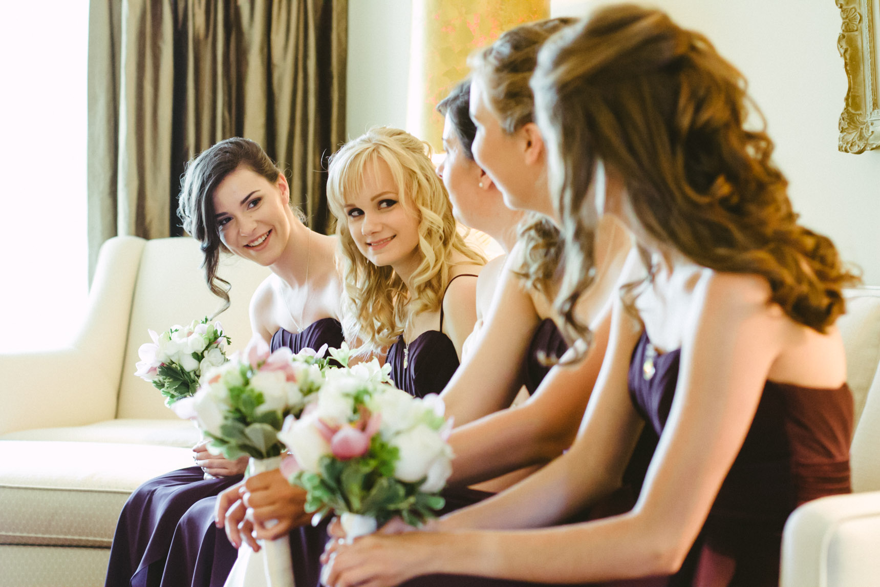 Bridesmaids sit in a row on a coach.
