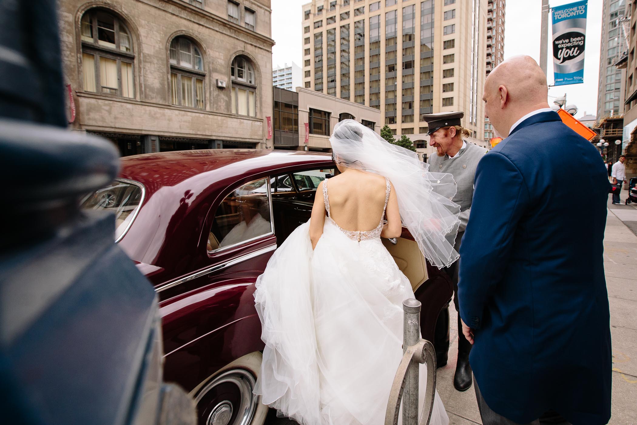 The bride entering a red Rolls Royce limo after wedding ceremony at Church of the Redeemer in Toronto.